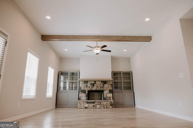 living room with beam ceiling, a stone fireplace, light hardwood / wood-style floors, and ceiling fan