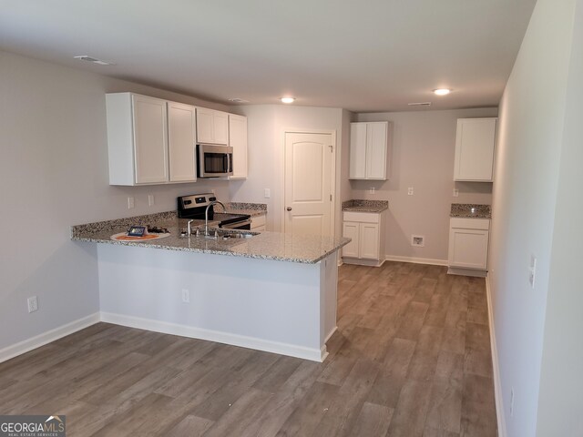 kitchen with appliances with stainless steel finishes, white cabinets, light stone counters, and light hardwood / wood-style floors