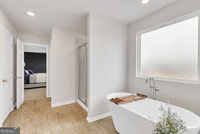 ensuite bathroom featuring a stall shower, a freestanding bath, wood finished floors, and recessed lighting