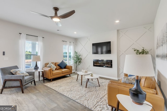 living room featuring recessed lighting, visible vents, light wood-style floors, a glass covered fireplace, and baseboards