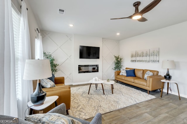 living room with visible vents, a ceiling fan, a glass covered fireplace, wood finished floors, and baseboards