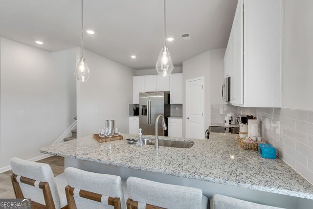 kitchen featuring visible vents, appliances with stainless steel finishes, white cabinetry, light stone countertops, and a peninsula