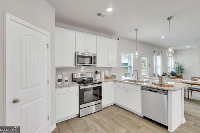 kitchen featuring visible vents, light wood-style flooring, appliances with stainless steel finishes, a sink, and a peninsula