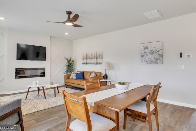 dining room featuring recessed lighting, baseboards, wood finished floors, and a glass covered fireplace