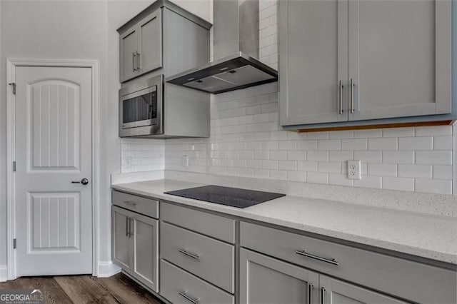 kitchen featuring stainless steel microwave, dark hardwood / wood-style flooring, wall chimney exhaust hood, light stone countertops, and tasteful backsplash