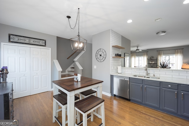 kitchen with dishwasher, backsplash, ceiling fan with notable chandelier, hardwood / wood-style floors, and sink