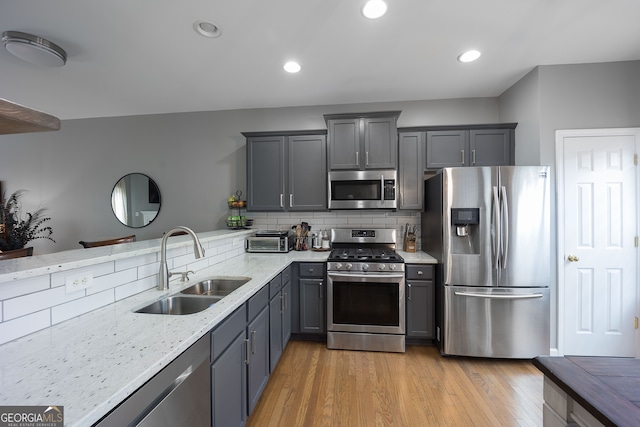 kitchen featuring appliances with stainless steel finishes, tasteful backsplash, sink, light wood-type flooring, and light stone countertops