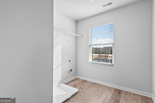 clothes washing area featuring light hardwood / wood-style flooring, electric dryer hookup, and plenty of natural light