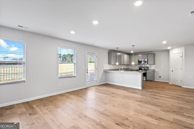 kitchen with gray cabinets, appliances with stainless steel finishes, pendant lighting, and light hardwood / wood-style floors