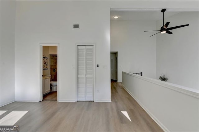 unfurnished bedroom with connected bathroom, light wood-type flooring, a high ceiling, and ceiling fan