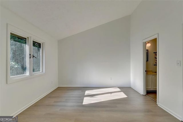 unfurnished bedroom featuring ensuite bathroom, wood-type flooring, and vaulted ceiling