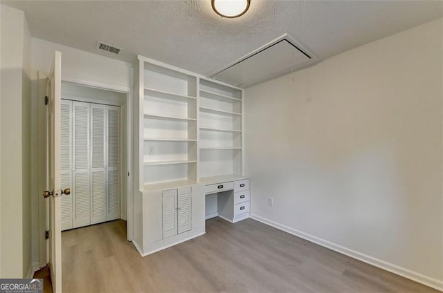 unfurnished office featuring wood-type flooring, a textured ceiling, and built in desk