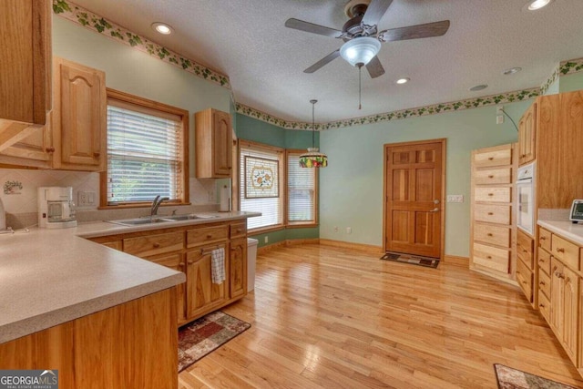 kitchen with white oven, sink, light hardwood / wood-style floors, and decorative backsplash