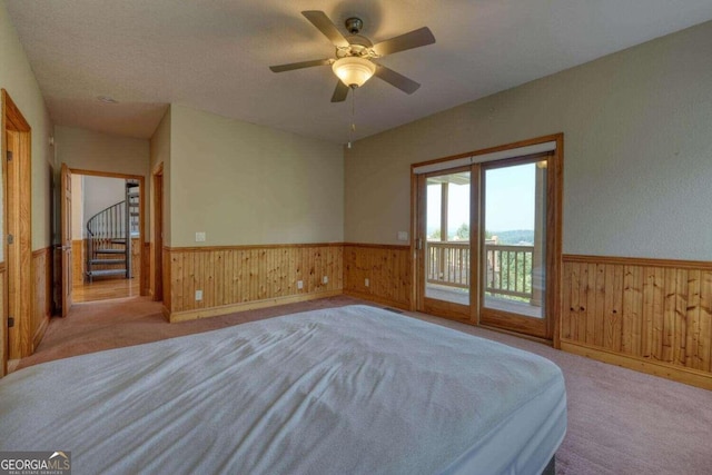 unfurnished bedroom with ceiling fan, wooden walls, light carpet, and access to outside