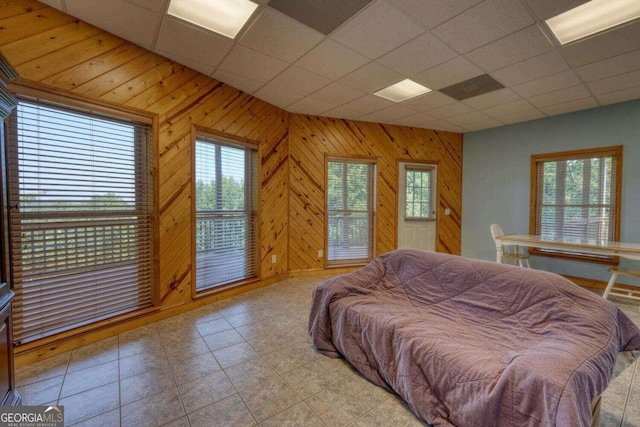 tiled bedroom with a paneled ceiling, multiple windows, and wood walls