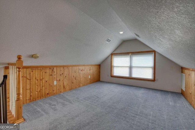 bonus room with lofted ceiling, a textured ceiling, carpet, and wood walls