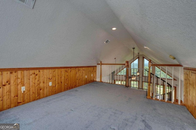 additional living space featuring lofted ceiling, carpet flooring, a textured ceiling, and wood walls