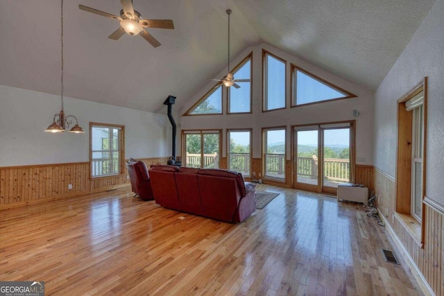 living room with a wood stove, ceiling fan with notable chandelier, high vaulted ceiling, and light hardwood / wood-style flooring