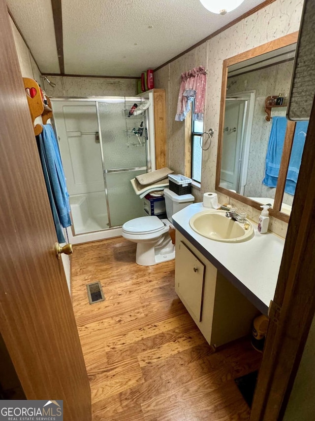 bathroom with a textured ceiling, hardwood / wood-style flooring, a shower with door, toilet, and vanity