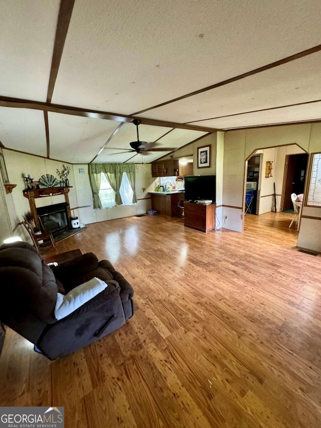 living room with hardwood / wood-style floors, lofted ceiling with beams, a textured ceiling, and ceiling fan