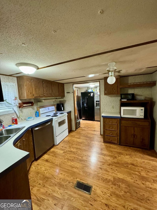 kitchen featuring light wood-type flooring, white appliances, a textured ceiling, dark brown cabinets, and sink