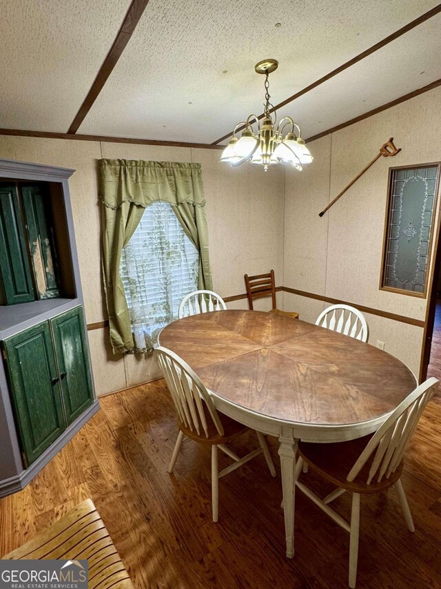 dining room with a textured ceiling, hardwood / wood-style flooring, a chandelier, and ornamental molding