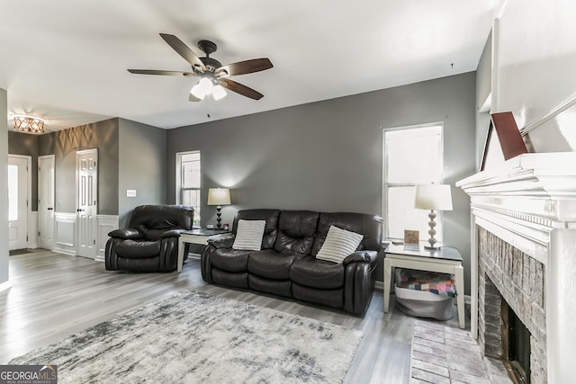 living room featuring a brick fireplace, ceiling fan, and light wood-type flooring