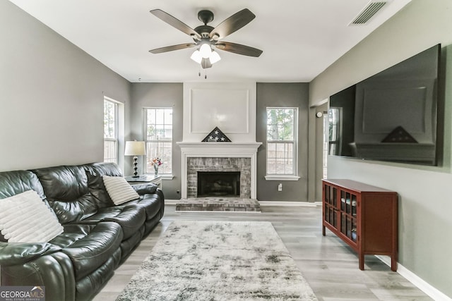 living room with a fireplace, a wealth of natural light, light hardwood / wood-style floors, and ceiling fan