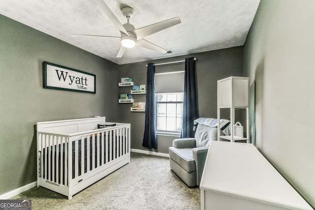 carpeted bedroom with ceiling fan, a nursery area, and a textured ceiling