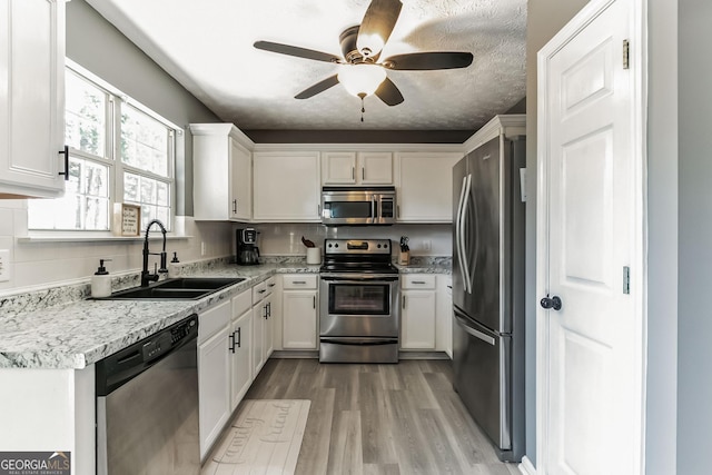 kitchen with appliances with stainless steel finishes, sink, white cabinets, and light hardwood / wood-style floors