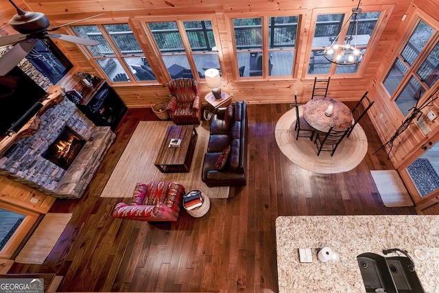 living room featuring wooden walls, a stone fireplace, hardwood / wood-style floors, and ceiling fan