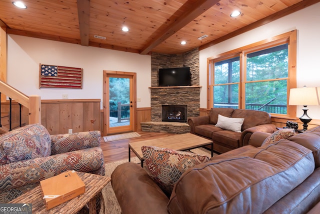 living room with wood-type flooring, a stone fireplace, and wood ceiling