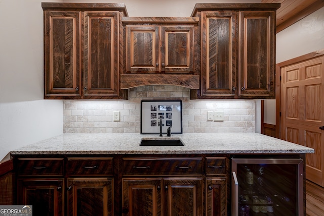 kitchen featuring dark brown cabinets, beverage cooler, light stone countertops, sink, and decorative backsplash