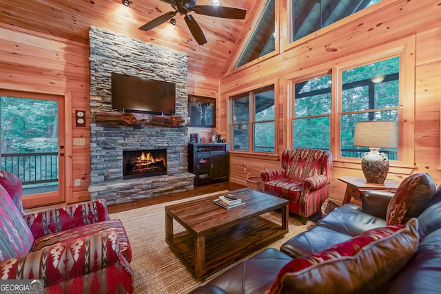 living room with wooden ceiling, a stone fireplace, wooden walls, hardwood / wood-style flooring, and ceiling fan