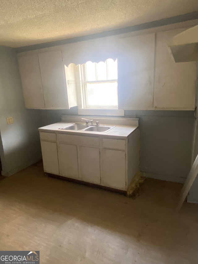 kitchen with a textured ceiling, white cabinets, sink, and light hardwood / wood-style floors