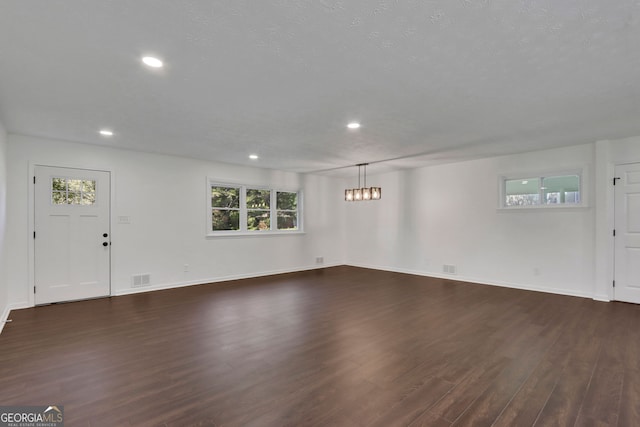 unfurnished living room with a textured ceiling, dark hardwood / wood-style flooring, and an inviting chandelier