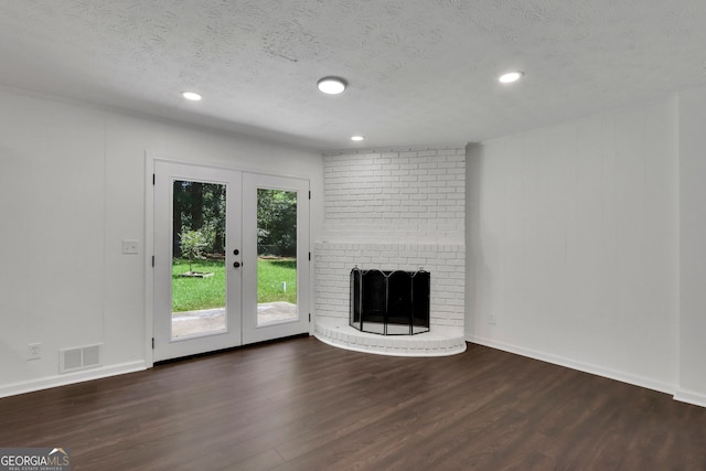 unfurnished living room featuring a brick fireplace, a textured ceiling, french doors, and wood-type flooring