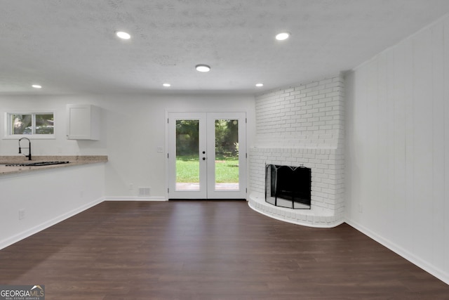 unfurnished living room with a brick fireplace, dark hardwood / wood-style floors, sink, french doors, and brick wall