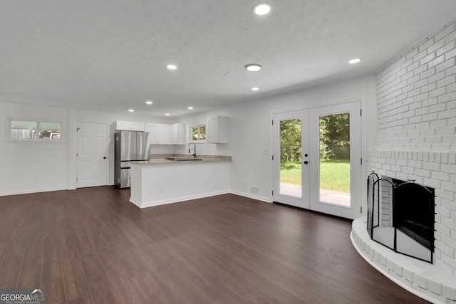 unfurnished living room featuring french doors, a textured ceiling, a brick fireplace, sink, and dark wood-type flooring