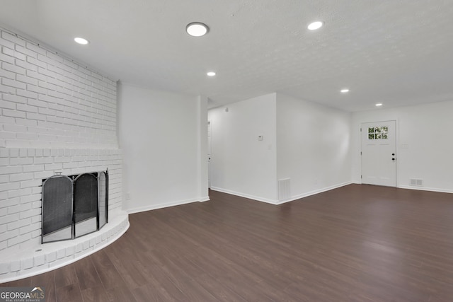 unfurnished living room featuring a textured ceiling, hardwood / wood-style floors, and a brick fireplace