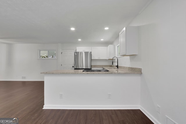 kitchen featuring appliances with stainless steel finishes, white cabinetry, light stone counters, hardwood / wood-style flooring, and kitchen peninsula