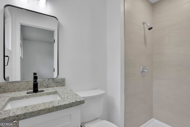 bathroom with tiled shower, vanity, and toilet