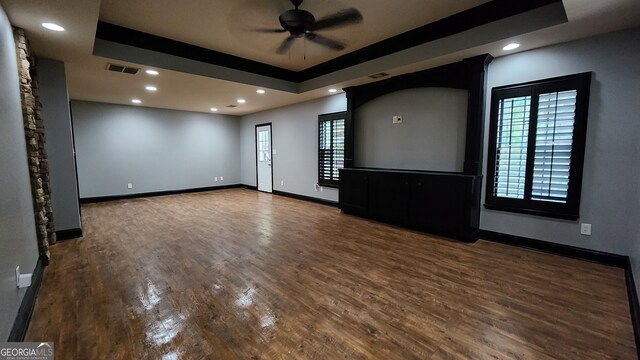 unfurnished living room with ceiling fan, a wealth of natural light, hardwood / wood-style flooring, and a tray ceiling