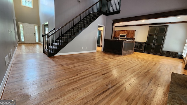 unfurnished living room with beam ceiling, light hardwood / wood-style flooring, and a high ceiling