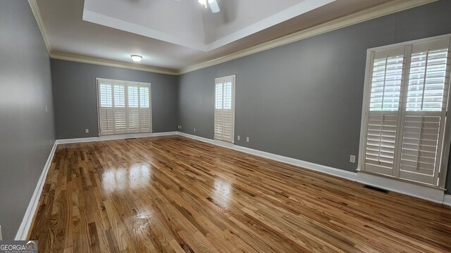 unfurnished room with ceiling fan, a raised ceiling, hardwood / wood-style floors, and crown molding