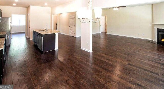 kitchen with a center island with sink, ceiling fan with notable chandelier, dark wood-type flooring, and sink