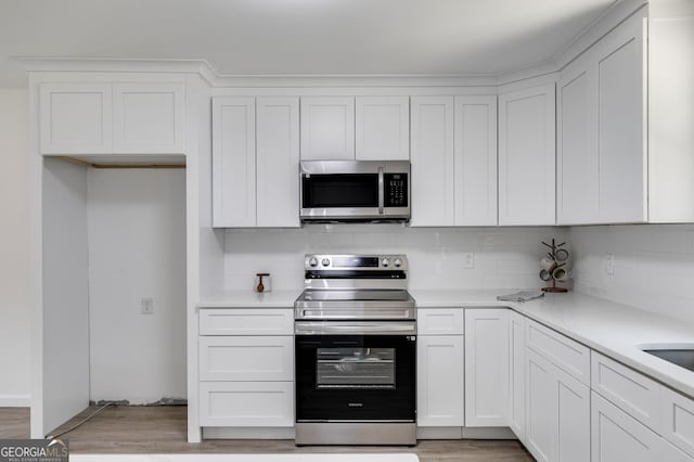 kitchen with appliances with stainless steel finishes, tasteful backsplash, light hardwood / wood-style flooring, and white cabinets