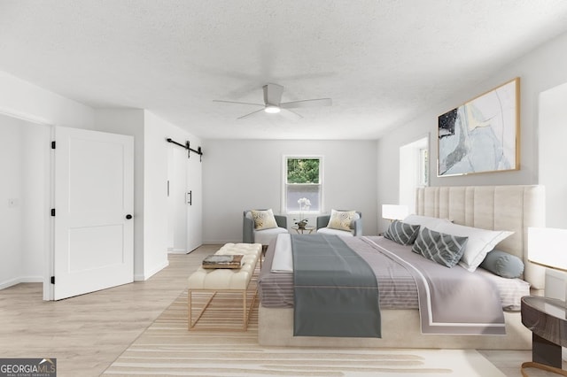 bedroom with ceiling fan, light hardwood / wood-style flooring, a barn door, and a textured ceiling