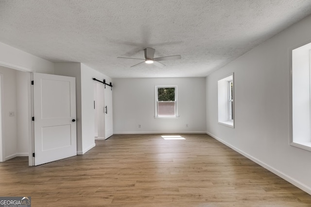 unfurnished bedroom featuring ceiling fan, a barn door, light hardwood / wood-style flooring, and a textured ceiling