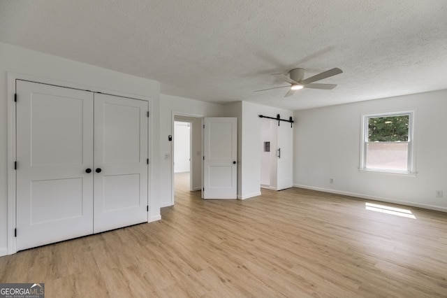 unfurnished bedroom featuring light wood-type flooring, a barn door, a closet, and ceiling fan